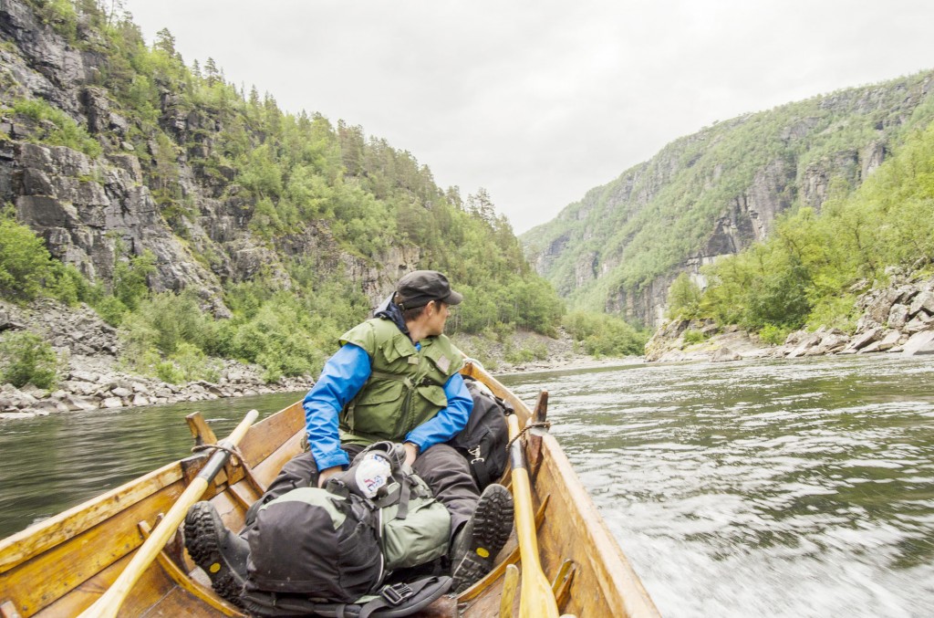 Både båtfører og passasjerer må følge nøye med når en ferdes med elvebåt i Altaelva. Her gjør en seg klar til å passere Pahtakoski, et lumskt fossestryk omkranset av berg på begge sider. • Alattionjovela oon kuljettava varovasti. Tässä jokivene sivvuuttaa kavalan Pahtakosken missä joki pakkaanttuu korkkeitten pahtojen välistä.